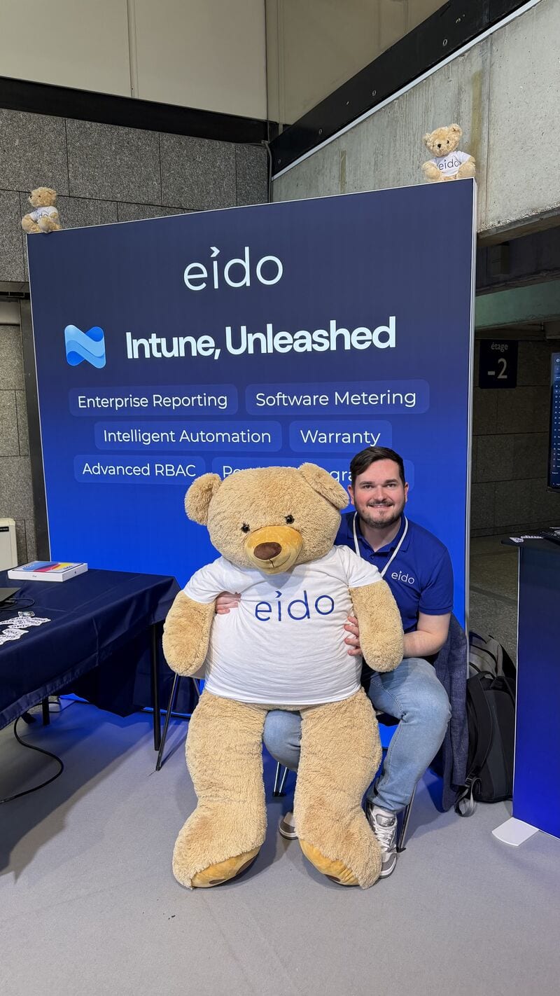 One of the Eido team sitting behind Odie, a large teddy bear, at the Eido stand.